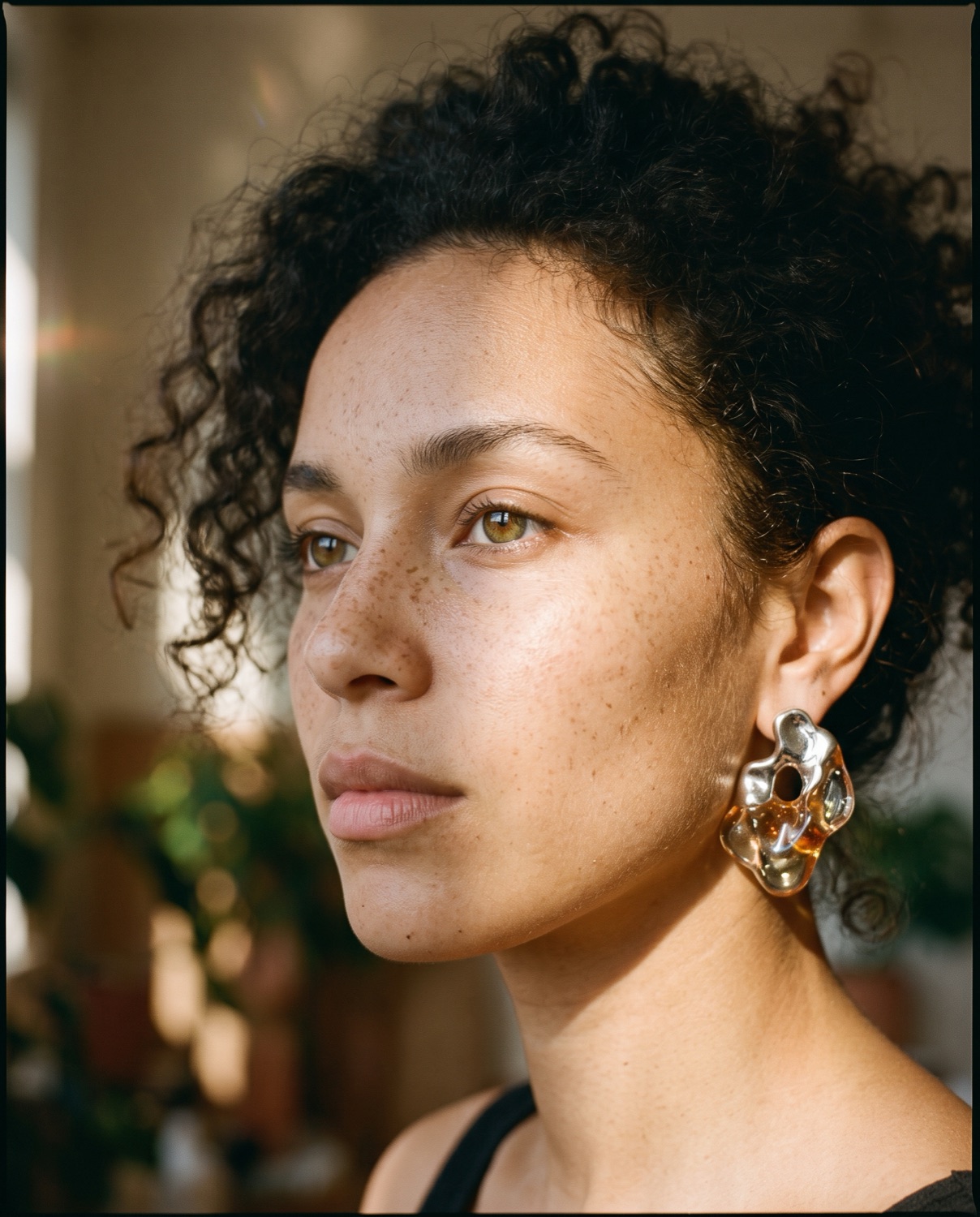 Freckled Editorial Portrait — Close-up editorial portrait of a diverse woman with sharp jawline and natural freckles, wearing avant-garde sculptural earrings made of translucent resin and molten silver.